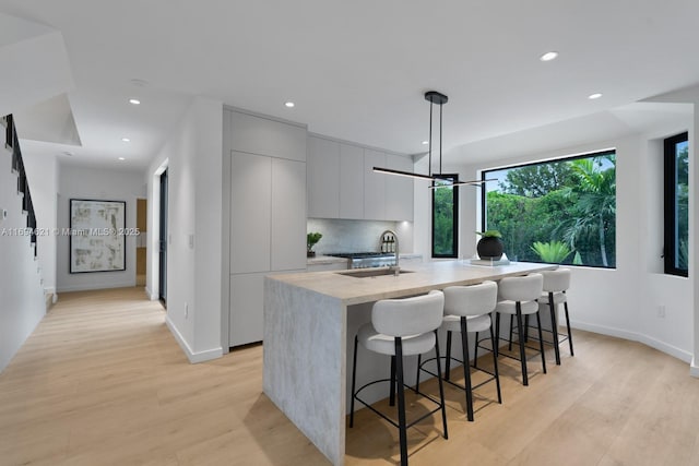 kitchen with pendant lighting, a center island with sink, a kitchen breakfast bar, sink, and light hardwood / wood-style floors