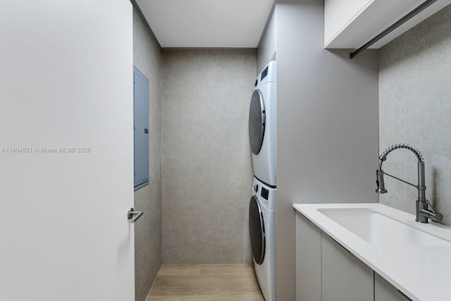 laundry area featuring light wood-type flooring, sink, and stacked washer and clothes dryer