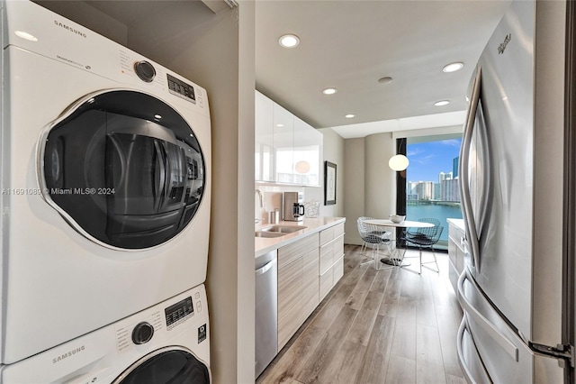 clothes washing area featuring stacked washer and clothes dryer, a water view, sink, and light hardwood / wood-style flooring