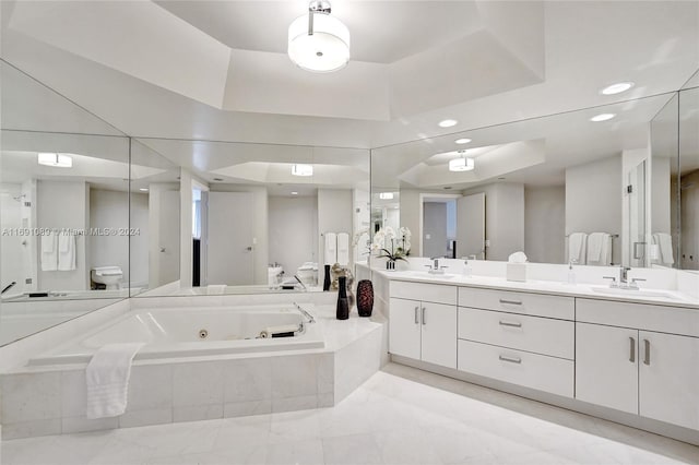 bathroom featuring a tray ceiling, tiled tub, vanity, and toilet