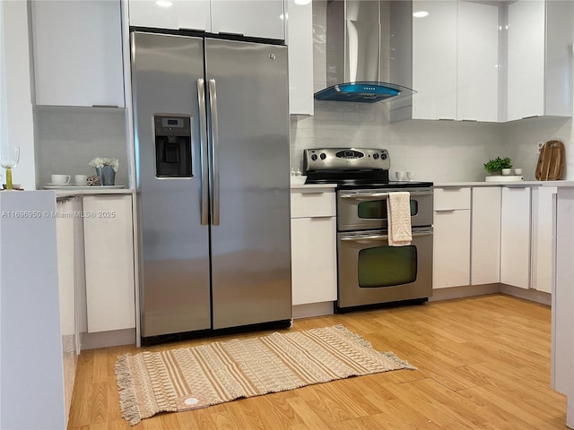 kitchen with white cabinetry, stainless steel appliances, tasteful backsplash, light hardwood / wood-style floors, and ventilation hood