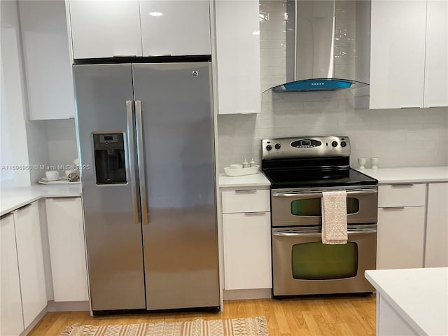 kitchen with tasteful backsplash, appliances with stainless steel finishes, wall chimney exhaust hood, and white cabinetry