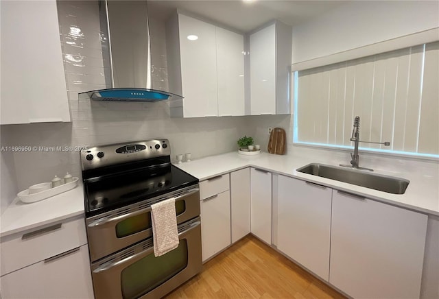 kitchen featuring wall chimney range hood, light hardwood / wood-style floors, double oven range, sink, and white cabinetry