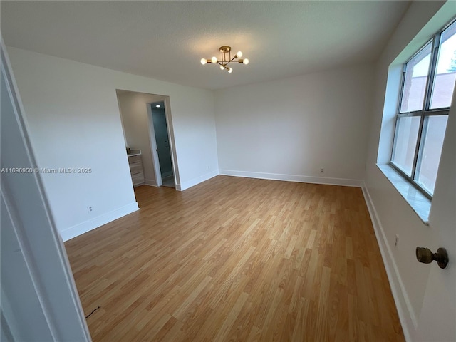 empty room featuring an inviting chandelier and light wood-type flooring