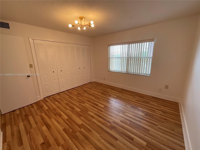 unfurnished bedroom featuring a textured ceiling, a closet, hardwood / wood-style flooring, and a notable chandelier