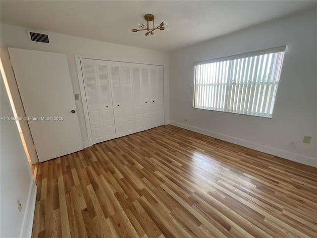 unfurnished bedroom featuring light wood-type flooring, a closet, and an inviting chandelier