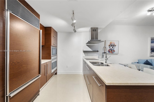 kitchen with sink, rail lighting, built in appliances, wall chimney exhaust hood, and light tile patterned floors