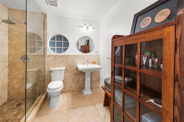 bathroom with sink, tile patterned floors, tiled shower, toilet, and tile walls