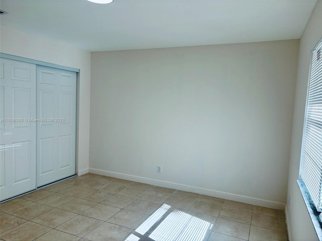 unfurnished bedroom with multiple windows, light tile patterned flooring, and a closet