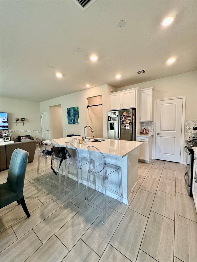 kitchen featuring a kitchen bar, appliances with stainless steel finishes, white cabinetry, and an island with sink