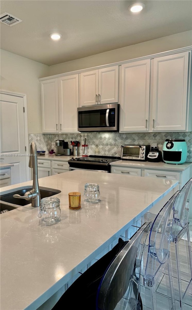 kitchen featuring tasteful backsplash, white cabinetry, a kitchen bar, and stainless steel appliances