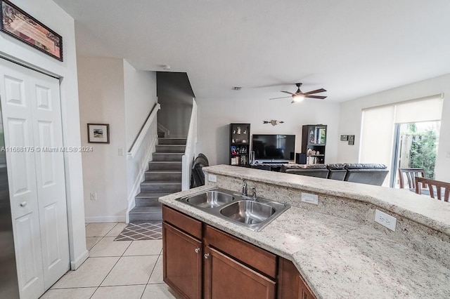 kitchen with light stone countertops, light tile patterned floors, ceiling fan, and sink