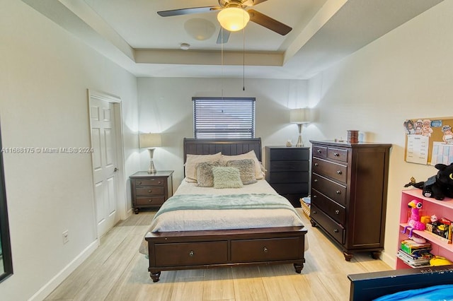 bedroom featuring light wood-type flooring, a tray ceiling, and ceiling fan