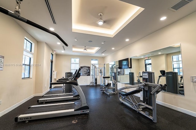 exercise room with ceiling fan, a raised ceiling, and plenty of natural light