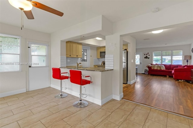 kitchen featuring a kitchen bar, decorative backsplash, light wood-type flooring, stainless steel appliances, and dark stone countertops