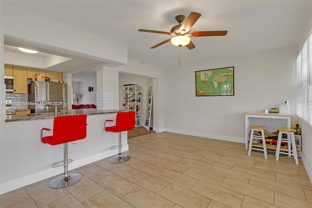 kitchen with decorative backsplash, ceiling fan, appliances with stainless steel finishes, kitchen peninsula, and a breakfast bar area