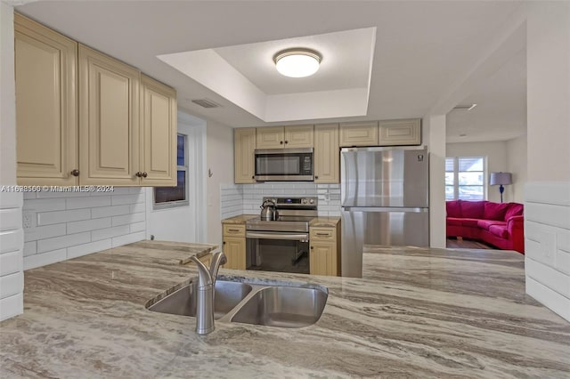 kitchen with stainless steel appliances, a raised ceiling, tasteful backsplash, and sink