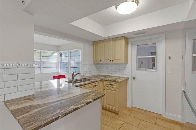 kitchen featuring kitchen peninsula, backsplash, dark stone counters, and sink