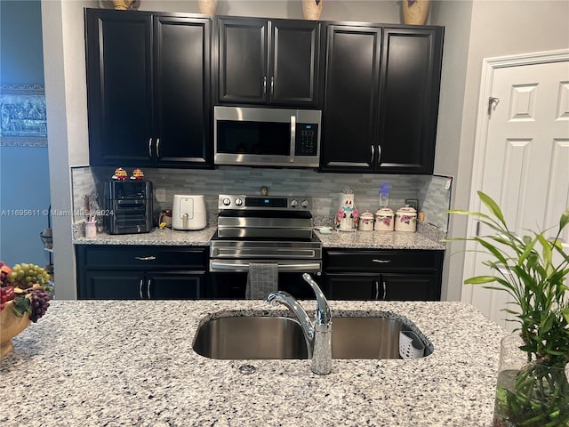 kitchen featuring tasteful backsplash, light stone countertops, sink, and appliances with stainless steel finishes