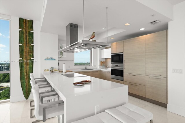 kitchen featuring a kitchen breakfast bar, island range hood, plenty of natural light, and black appliances