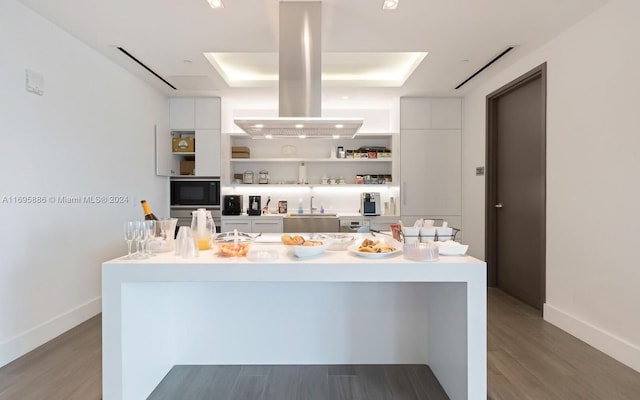 kitchen featuring island exhaust hood, a raised ceiling, dark hardwood / wood-style floors, and white cabinetry