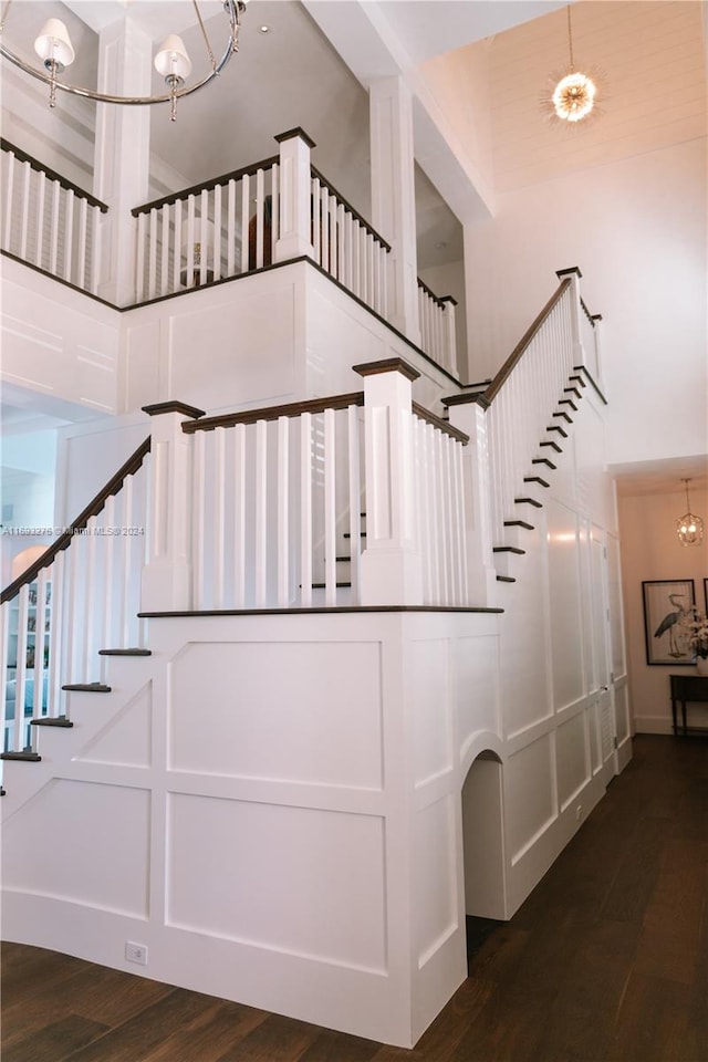 stairway featuring hardwood / wood-style floors, a towering ceiling, and an inviting chandelier