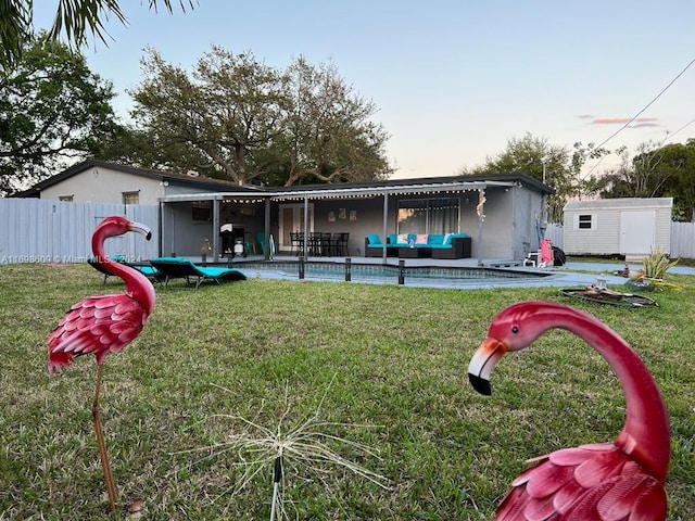 back house at dusk with a yard, an outdoor living space, a storage unit, and a patio area