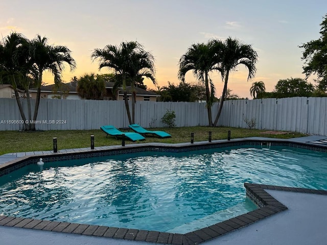 pool at dusk featuring a yard