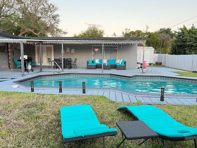 pool at dusk with a lawn, a storage unit, an outdoor hangout area, grilling area, and a patio