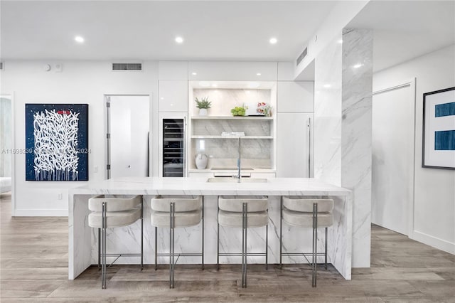 kitchen with a breakfast bar, light hardwood / wood-style flooring, white cabinetry, and beverage cooler