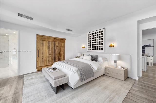 bedroom with connected bathroom and light hardwood / wood-style floors