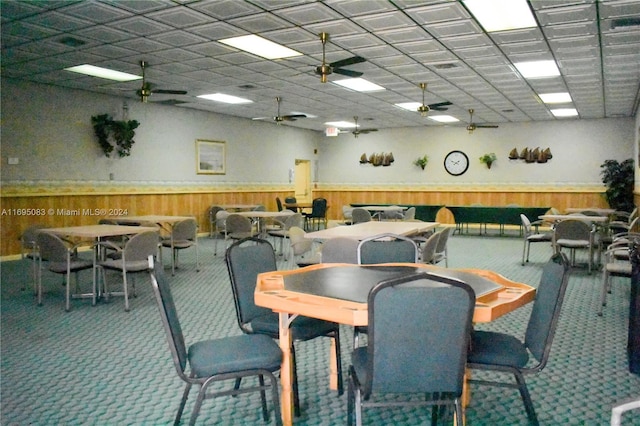 dining room with carpet flooring, ceiling fan, a drop ceiling, and wooden walls