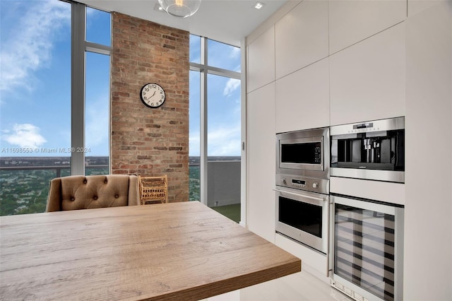 kitchen featuring floor to ceiling windows, white cabinetry, stainless steel appliances, and beverage cooler