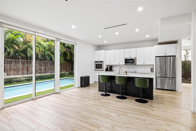 kitchen with white cabinetry, a kitchen breakfast bar, an island with sink, light hardwood / wood-style floors, and appliances with stainless steel finishes