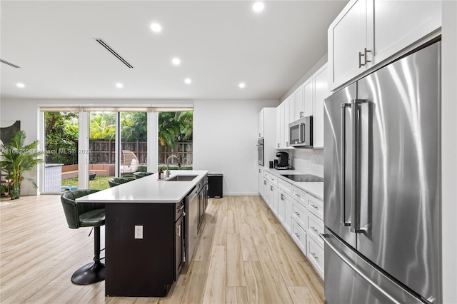 kitchen with white cabinetry, sink, stainless steel appliances, a kitchen bar, and a kitchen island with sink