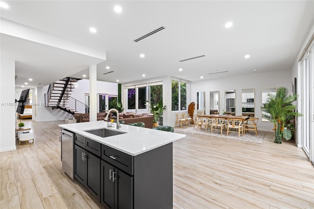 kitchen with a center island with sink, dishwasher, sink, and light hardwood / wood-style flooring