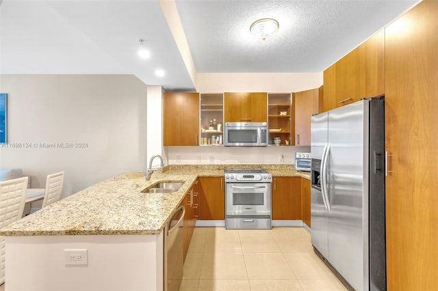 kitchen featuring kitchen peninsula, appliances with stainless steel finishes, light stone countertops, sink, and light tile patterned floors