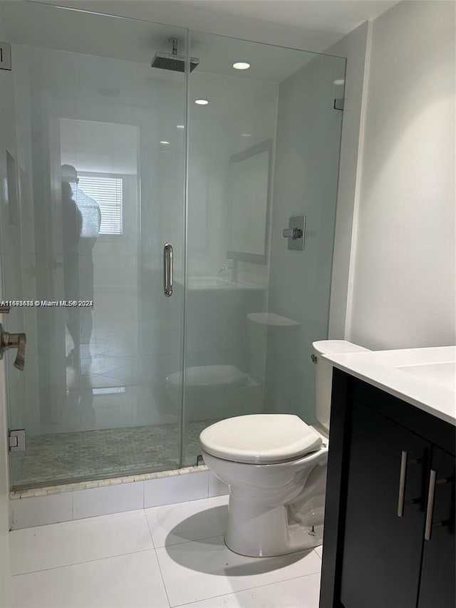 bathroom featuring tile patterned flooring, vanity, toilet, and a shower with door