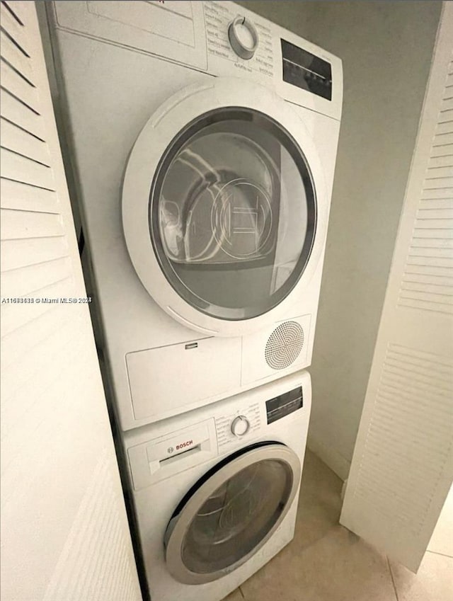 laundry area with light tile patterned floors and stacked washing maching and dryer