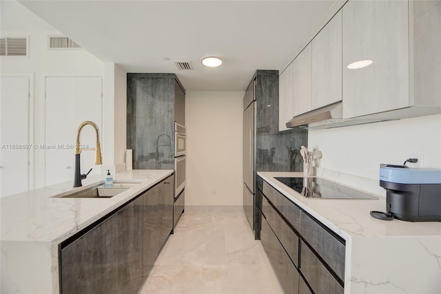 kitchen with gray cabinetry, light stone counters, sink, and black electric stovetop