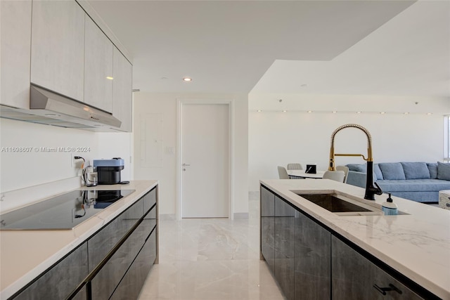 kitchen with light stone countertops, black electric stovetop, extractor fan, sink, and gray cabinets