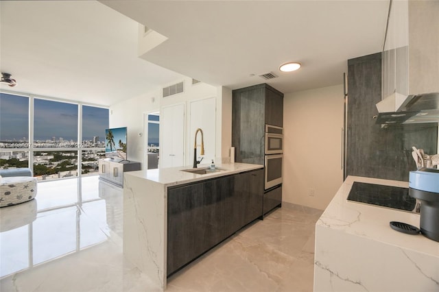 kitchen featuring exhaust hood, sink, black electric cooktop, light stone counters, and a wall of windows