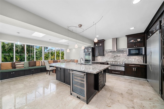 kitchen featuring a skylight, stainless steel appliances, an island with sink, decorative light fixtures, and dark brown cabinets