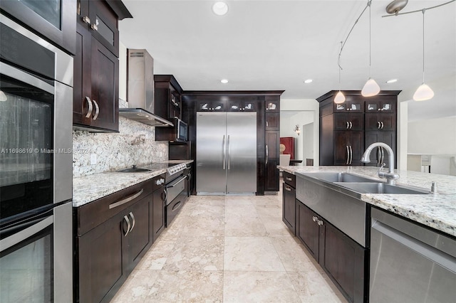 kitchen featuring dark brown cabinetry, wall chimney exhaust hood, hanging light fixtures, tasteful backsplash, and appliances with stainless steel finishes