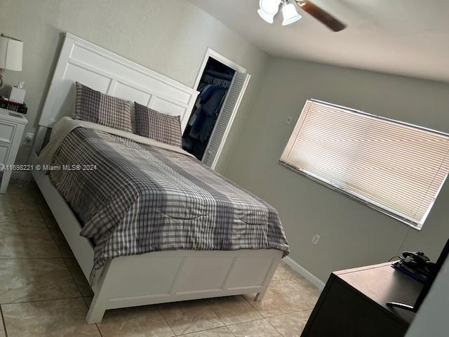 tiled bedroom with ceiling fan and a walk in closet