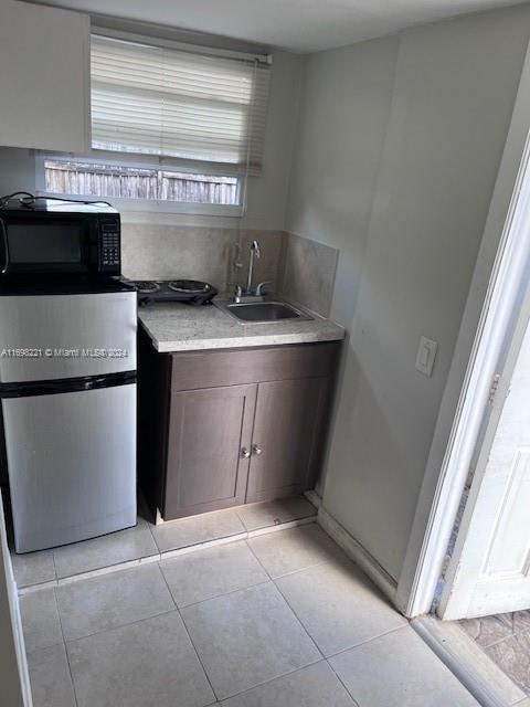 kitchen with dark brown cabinetry, stainless steel fridge, sink, and light tile patterned flooring