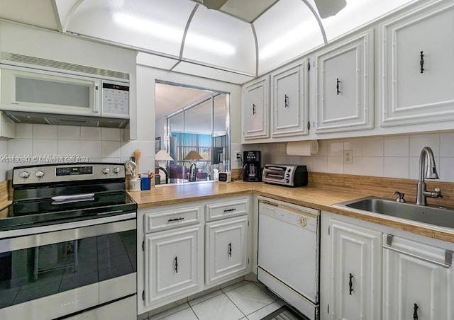 kitchen with white appliances, backsplash, white cabinetry, and sink