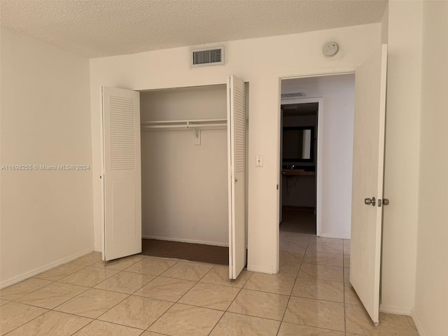 unfurnished bedroom featuring light tile patterned floors, a textured ceiling, and a closet