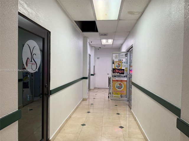 hall featuring light tile patterned floors and a paneled ceiling