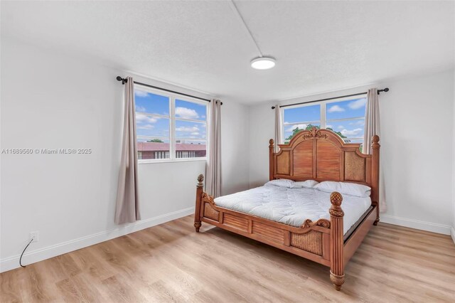 bedroom featuring a textured ceiling, light hardwood / wood-style flooring, and multiple windows